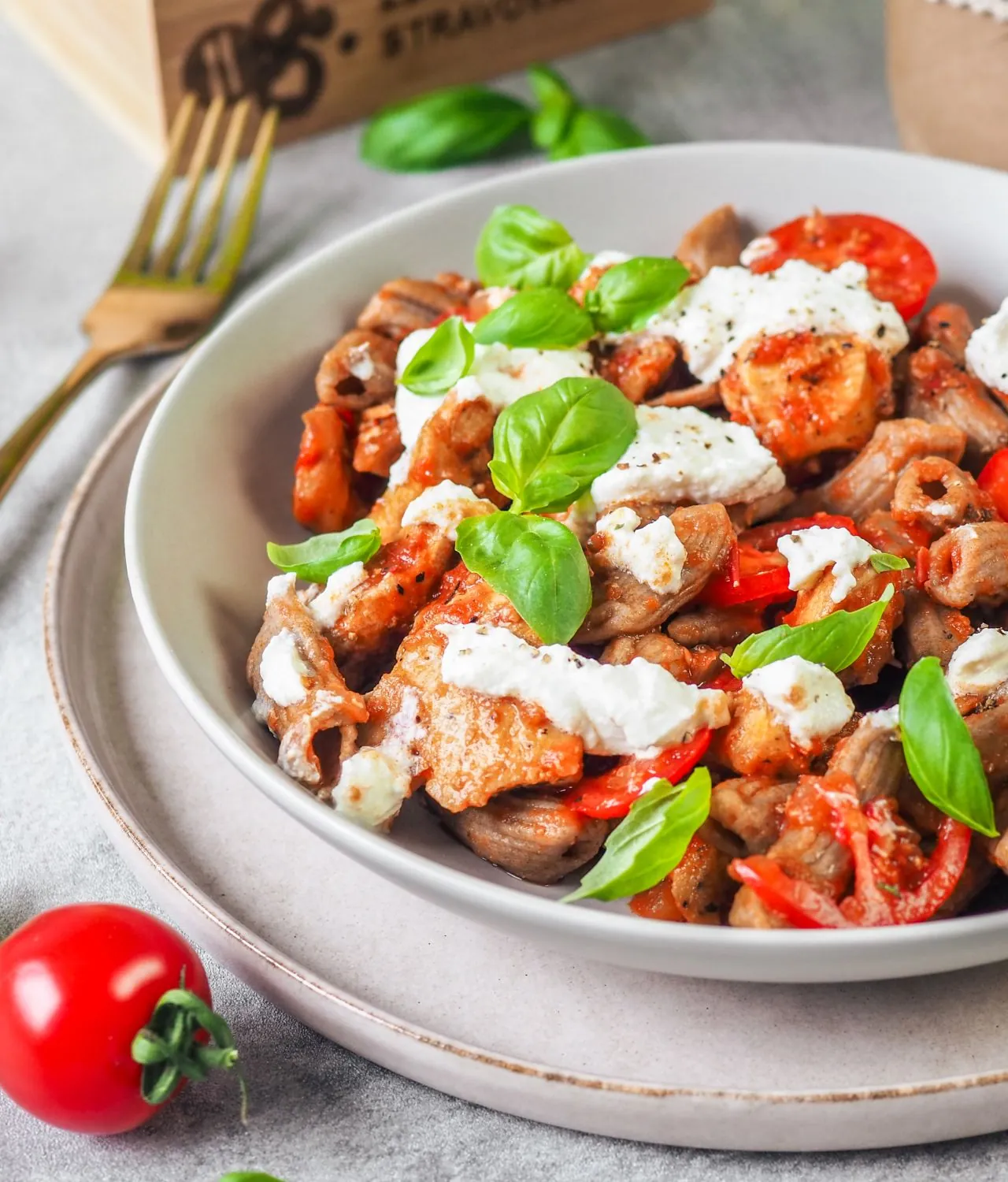 A bowl of chicken with tomatoes and ricotta, sprinkled with basil