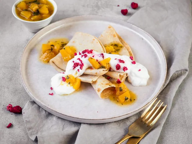 A plate of pancakes with peach sauce and sour cream